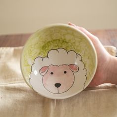 a hand holding a bowl with a sheep painted on it