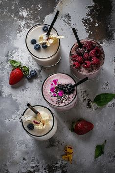 three glasses filled with different types of smoothies and fruit on top of a table