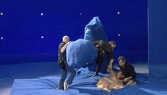 three men working on an elephant sculpture in a blue room with balls and lights around it