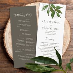 two wedding programs on top of a wooden table next to leaves and greenery in front of them