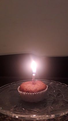 a cupcake with a single lit candle on it sitting on a glass platter