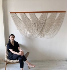 a woman is sitting on a chair in front of a wall hanging with white beads