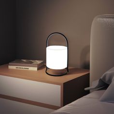 a white light sitting on top of a night stand next to a bed with pillows