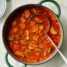 a pot filled with stew and carrots on top of a table next to a spoon