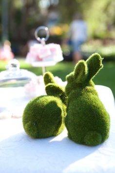 two moss covered bunnies sitting on top of a table next to a teapot