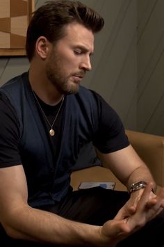 a man sitting on top of a brown couch next to a wooden wall and wearing a black shirt