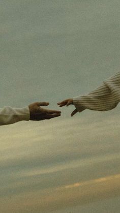 two hands reaching out towards each other in front of a sky with clouds and water