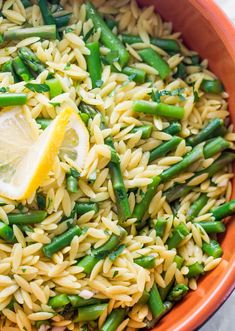 a bowl filled with pasta and asparagus on top of a table next to a lemon wedge