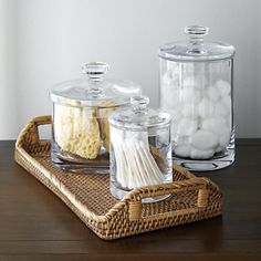 three glass containers filled with marshmallows on top of a wooden table next to a wicker basket