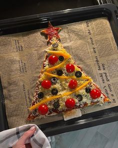 a pizza shaped like a christmas tree with tomatoes and olives on it, sitting on top of a newspaper