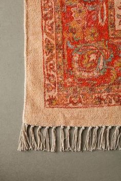 an orange and red rug with fringes on the bottom is laying on a gray surface