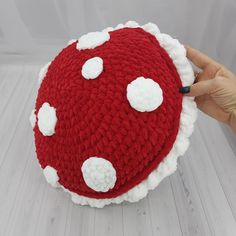 a hand holding a red and white knitted hat with polka dots on it's side