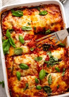 a white casserole dish filled with lasagna and basil