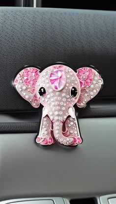 an elephant brooch sitting on the dashboard of a car with pink flowers in its trunk