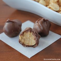 three pieces of chocolate covered peanut butter truffles on a napkin next to a bowl of peanuts