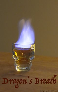 a glass cup filled with liquid sitting on top of a wooden table next to a lit candle