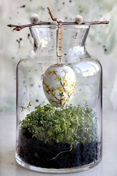 a glass vase with moss and an ornament in it on a table next to a window