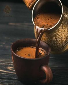 coffee being poured into a cup on top of a wooden table