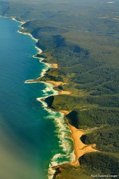 an aerial view of the ocean and coastline near some green land with trees on either side