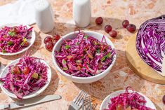 red cabbage and grapes are served in white bowls on a table with utensils