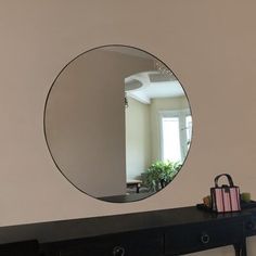 a mirror is hanging on the wall above a black dresser with a handbag and purse