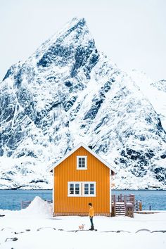 two people standing in front of a mountain with a yellow cabin on it's side