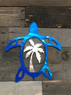 a blue metal turtle with a palm tree on it's back is mounted to a wooden wall