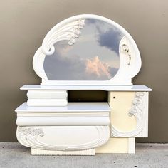 a white dresser with a mirror on top and clouds in the sky reflected in it