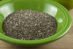 a green bowl filled with chia seeds on top of a wooden table next to an apple