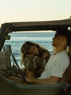 a man and woman are sitting in the back of a jeep with water in the background