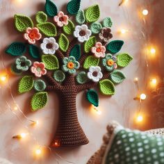 a crocheted tree with leaves and flowers is displayed on a white surface surrounded by string lights