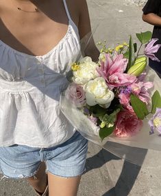 a woman holding a bouquet of flowers in her hand while standing on the side walk