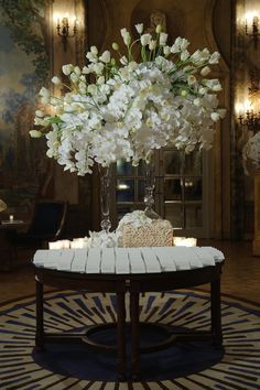 a vase filled with white flowers sitting on top of a table next to a rug