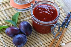 plums sit on a bamboo mat next to a jar of plum jam