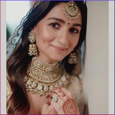 a woman in a bridal outfit smiling and holding her hands to her chest, wearing gold jewelry