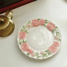 a white plate with pink roses on it next to a brass hook and a candle