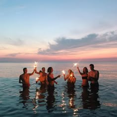 a group of people standing in the water holding sparklers