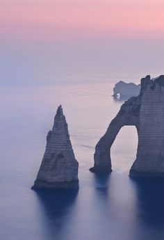 an arch shaped rock formation in the middle of water with two smaller rocks sticking out of it's sides