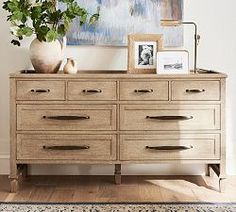 a wooden dresser sitting in front of a painting and potted plant on top of it