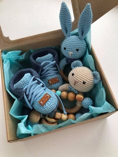 two crocheted stuffed animals in a box with blue shoes on the bottom and one is holding a wooden toy