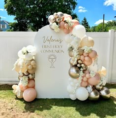 an arch with balloons and flowers on it in the grass next to a white fence