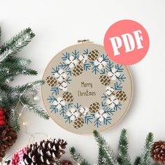 a cross stitch christmas ornament surrounded by pine cones and evergreen needles with the text pddf on it