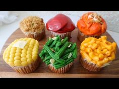 cupcakes decorated with different types of food on a wooden tray, including corn and carrots