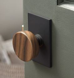 a wooden door knob on the side of a green door with a white bed in the background