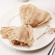 two pieces of cloth on a white plate with silverware and utensils next to it