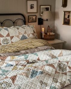 a bed with a quilt on top of it next to a night stand and lamp