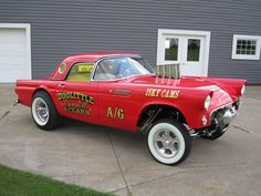 an old red car parked in front of a garage