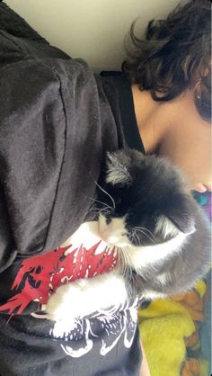 a woman laying on top of a bed next to a black and white cat