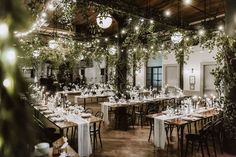 an indoor dining area with tables and chairs covered in greenery, surrounded by hanging lights