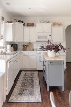 a large kitchen with white cabinets and wood flooring, along with a rug on the floor